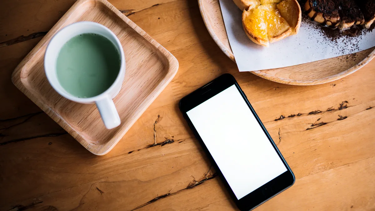 A phone resting on a marble cafe table next to a cup of black coffee.