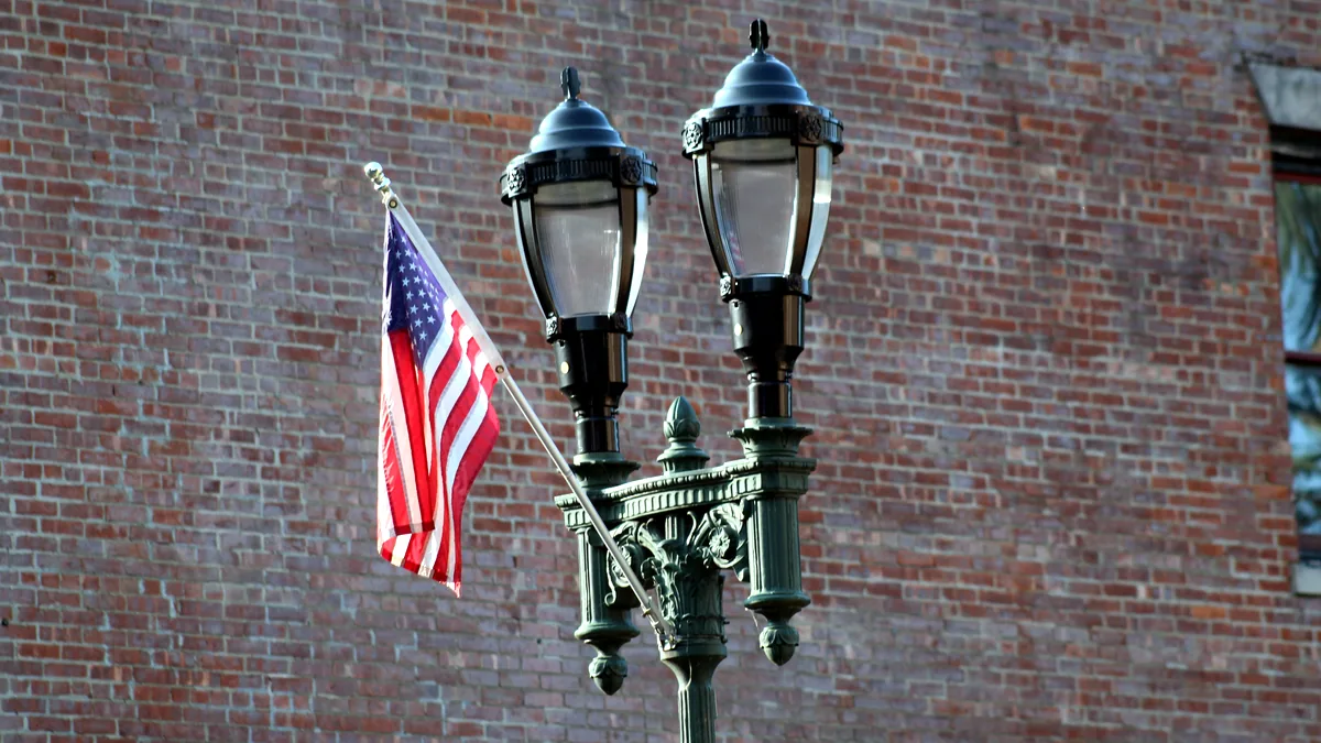 A small American flag mounted on a city lamppost with a blurred street behind.