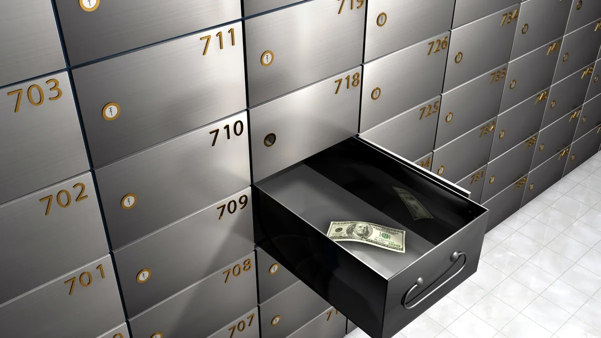 Rows of open safe deposit boxes in a dim vault with a single warm lamp.