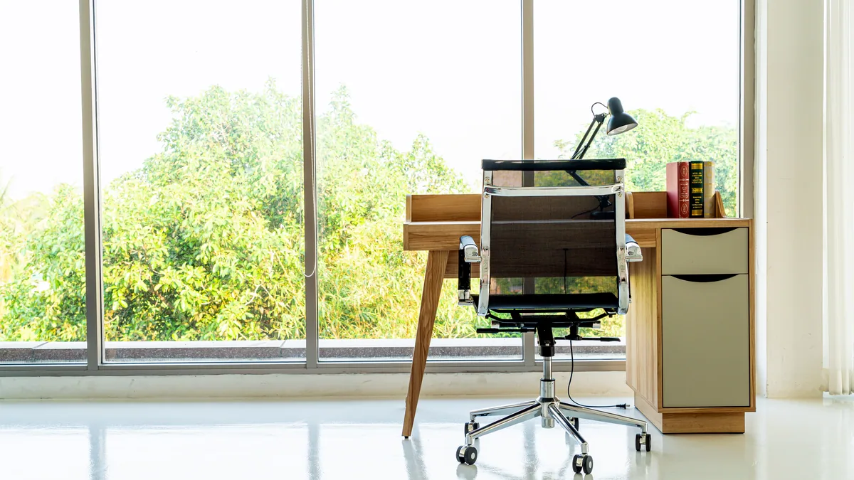 An empty office chair beside a window where morning light falls across the desk.