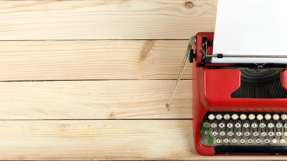 An old typewriter on a wooden desk with a sheet of paper still in the carriage.